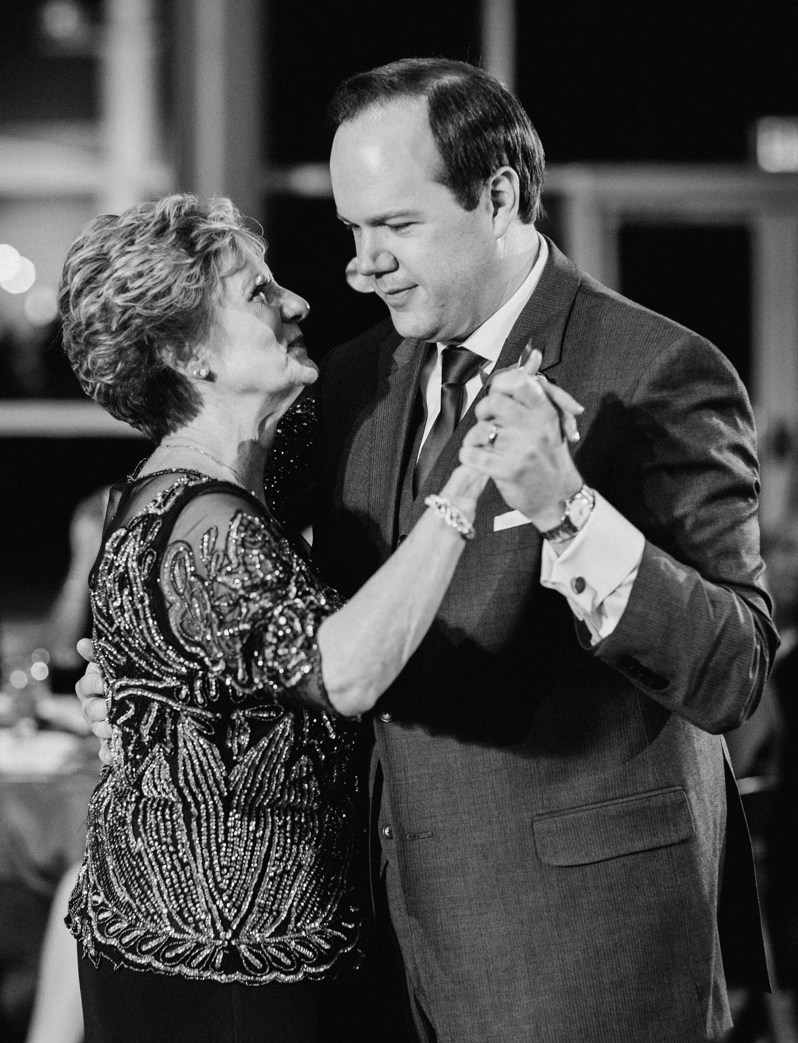 A greyscale photo of an older woman dancing with a man in formal apparel