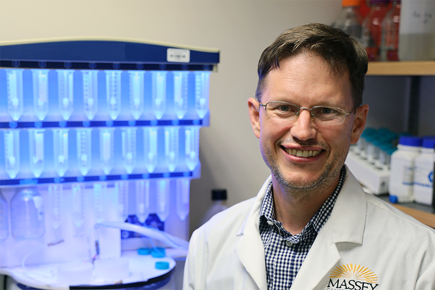 Man in glasses in lab with Massey branded white jacket smiling at camera